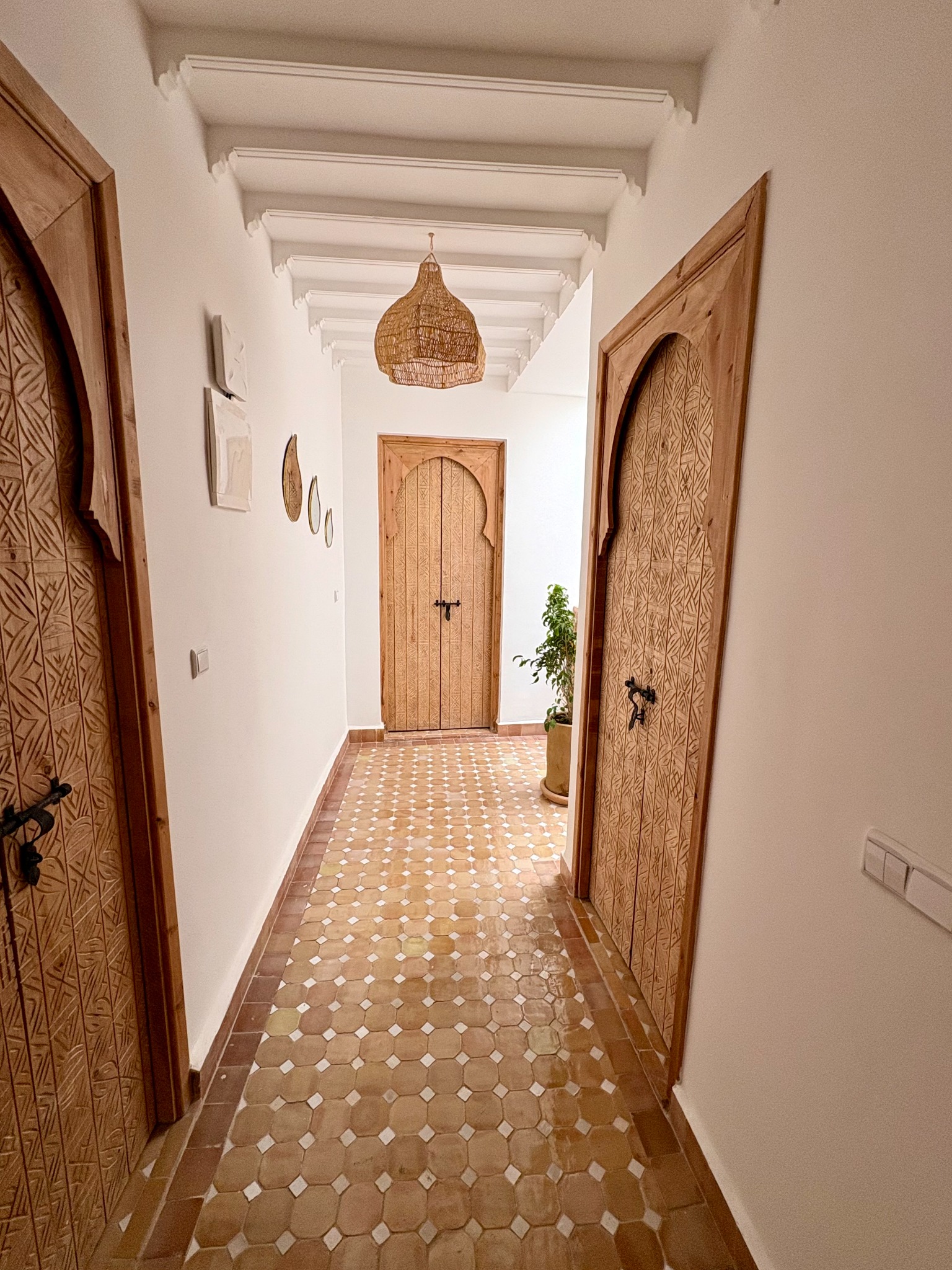 Couloir du riad aux portes en bois sculpté, sol en zelliges et suspension tressée